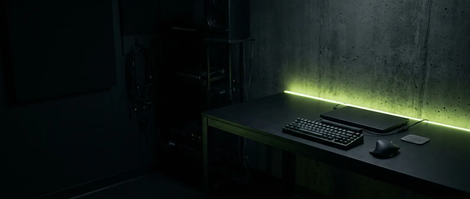 A dark, quiet desk with a keyboard and a closed laptop, lit by a lime strip light